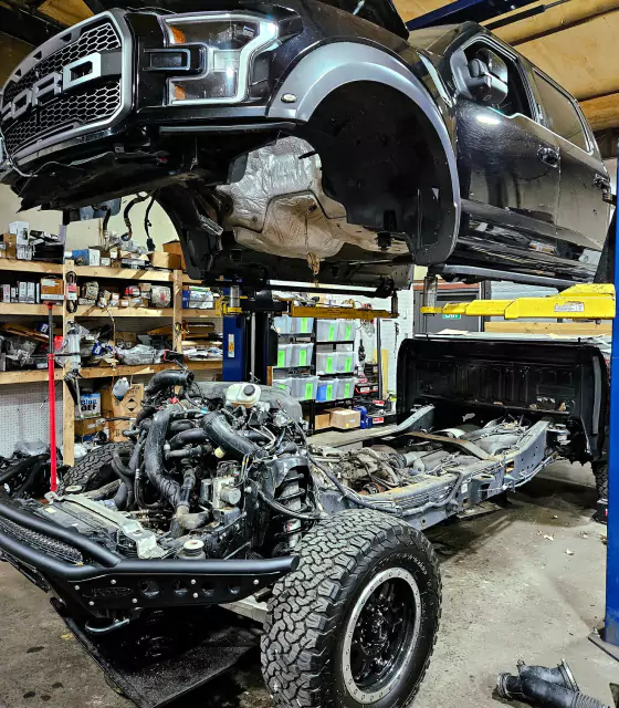 a car on a lift in a garage, Black Ford truck in the service bay at TruckWorks Garage receiving repair and maintenance.