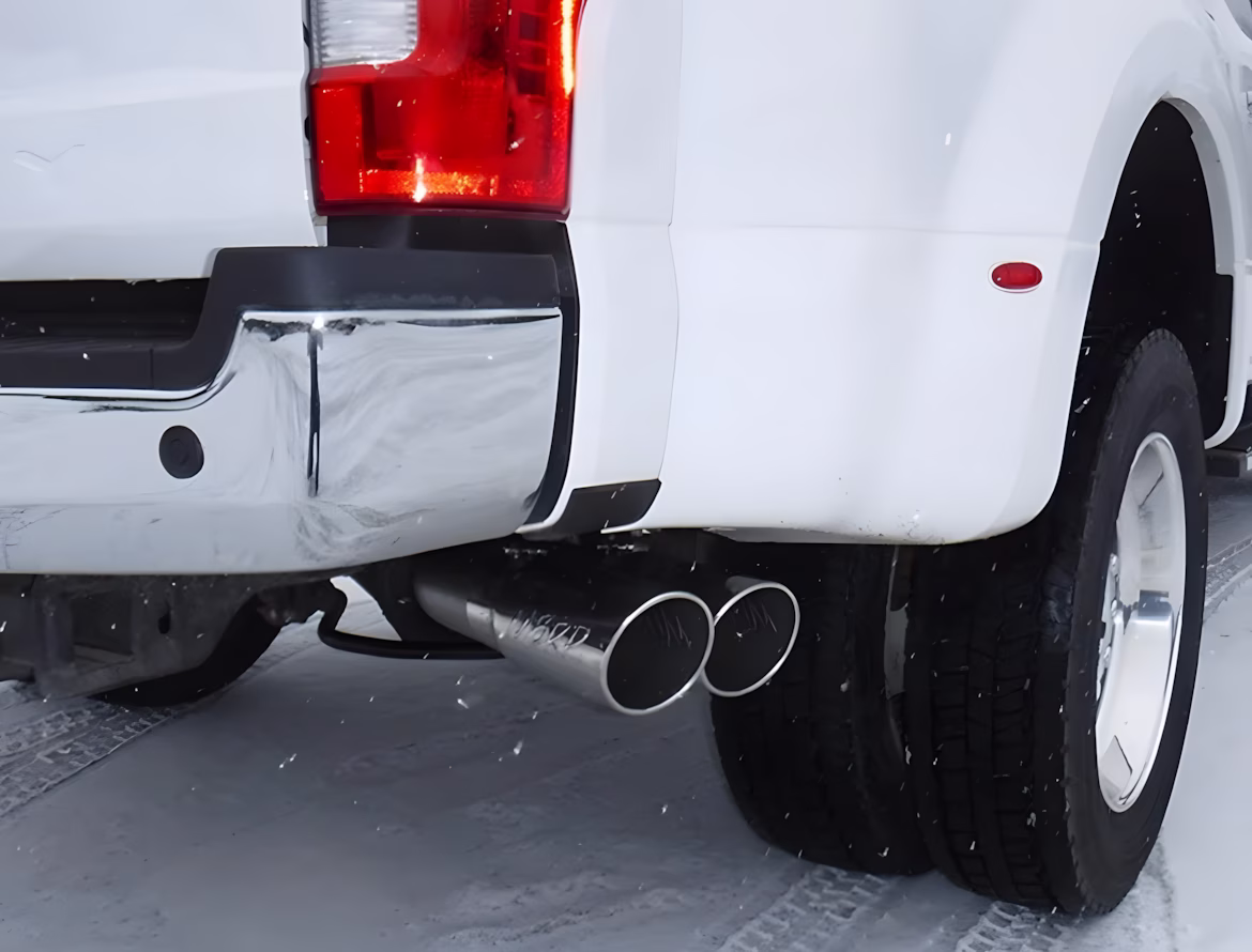 Truck's rear end with dual exhaust pipes parked on snowy surface.