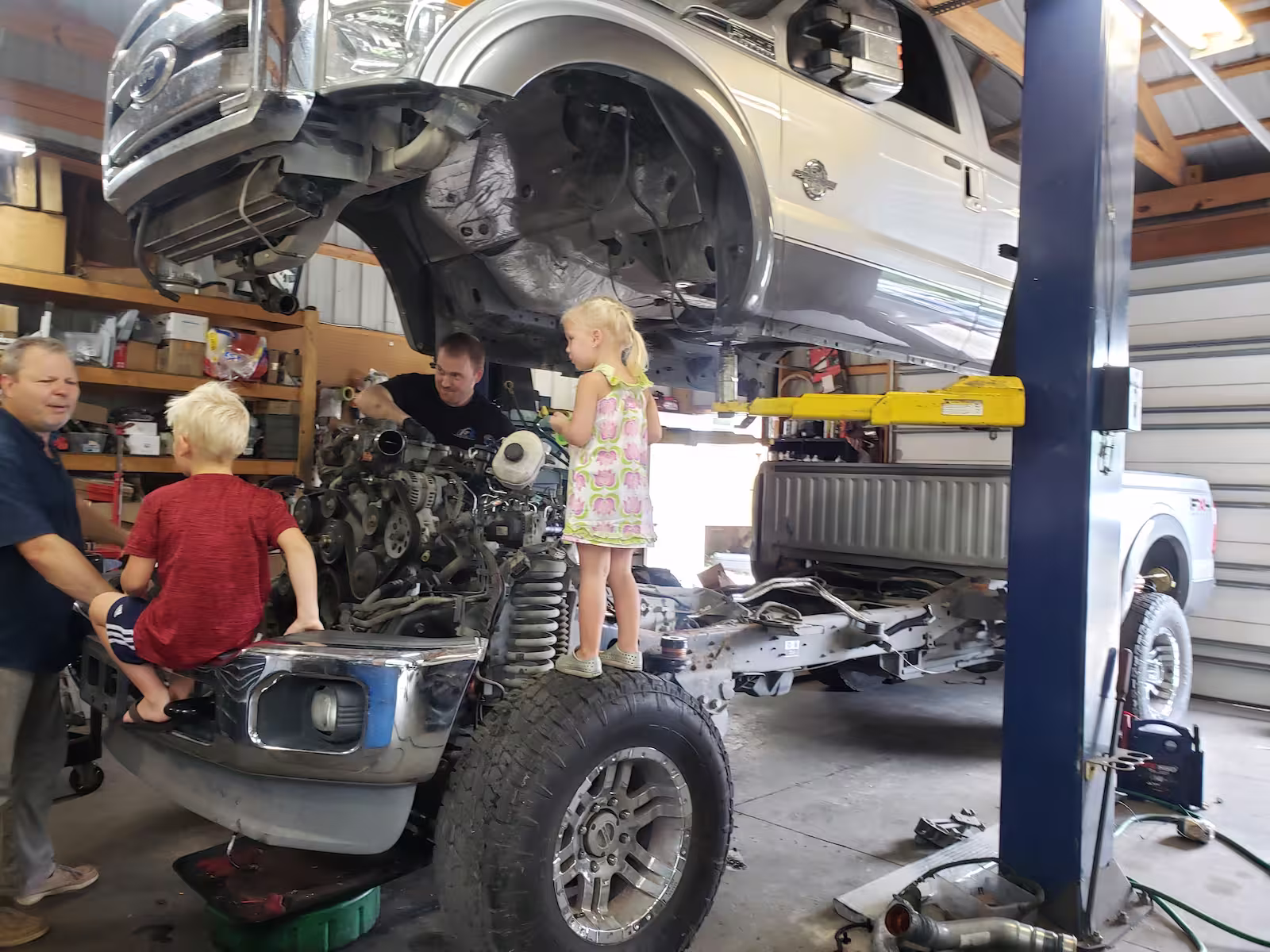 Truck on a hydraulic lift in a garage with people working on it.